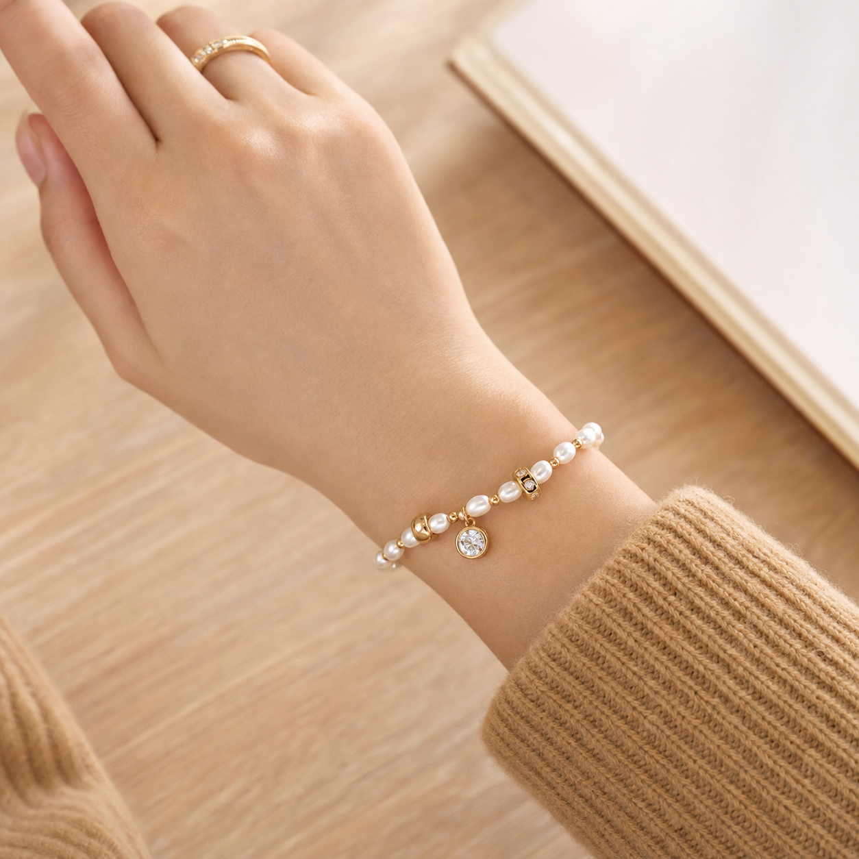 Close wrist view of the Vintage Gold pearl charm bracelet with a tan knit