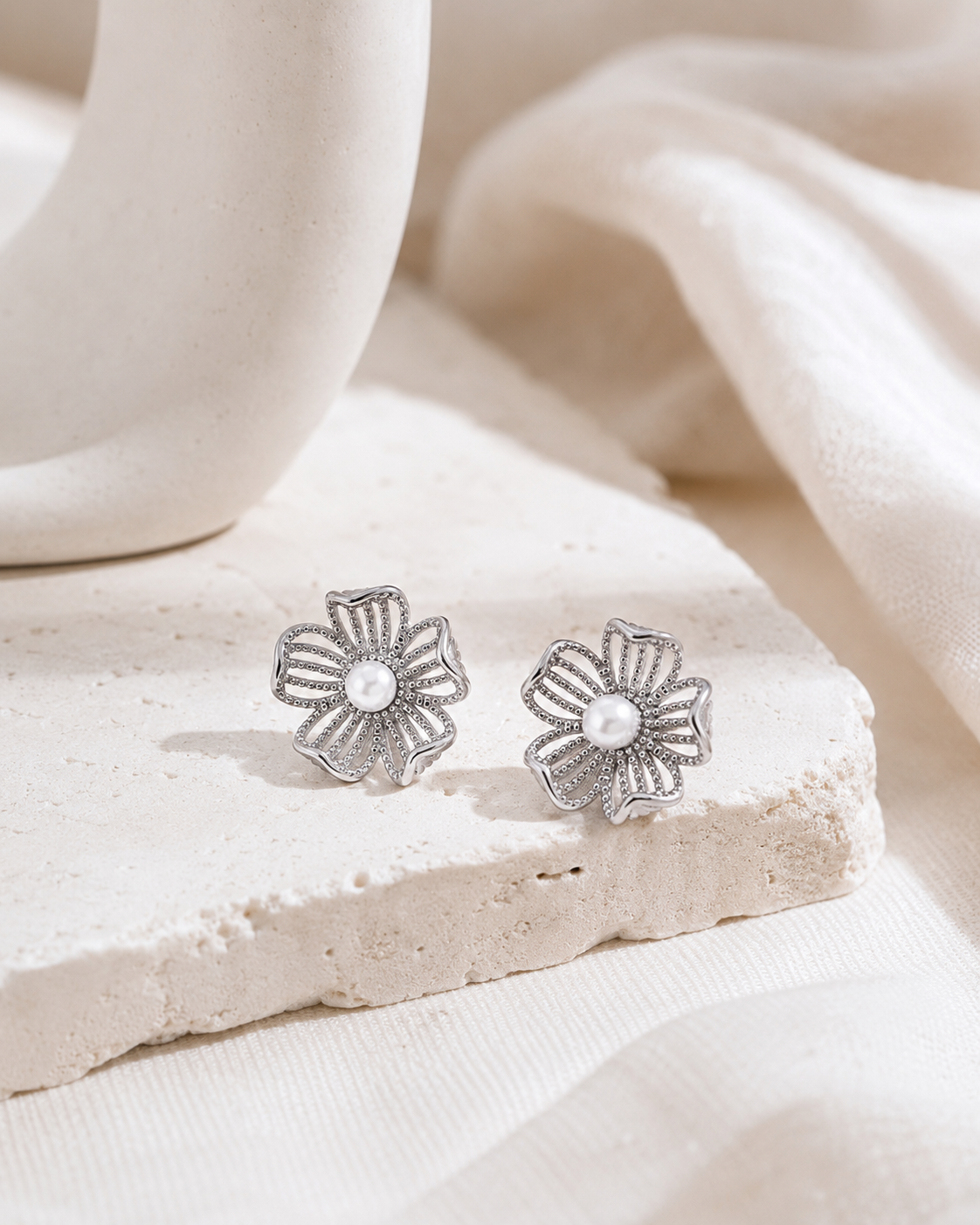Silver floral pearl stud earrings on a neutral display