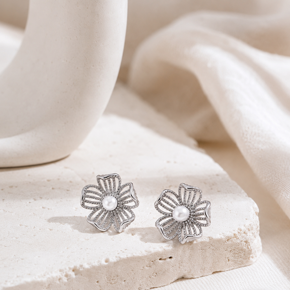 Silver floral pearl stud earrings on a neutral display