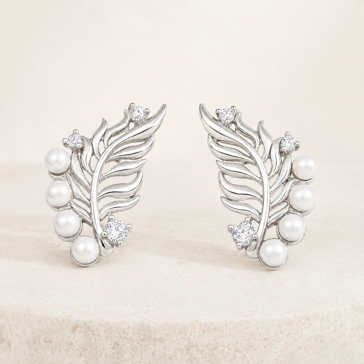 Pair of Silver feather pearl stud earrings with cubic zirconia on a stone display