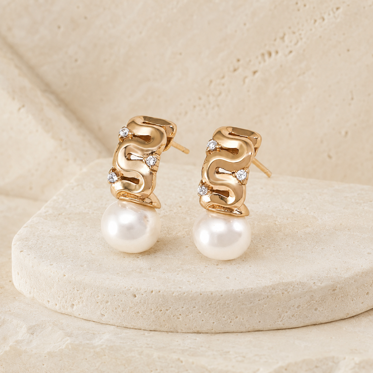 Vintage Gold pearl ribbon stud earrings with cubic zirconia on a stone display
