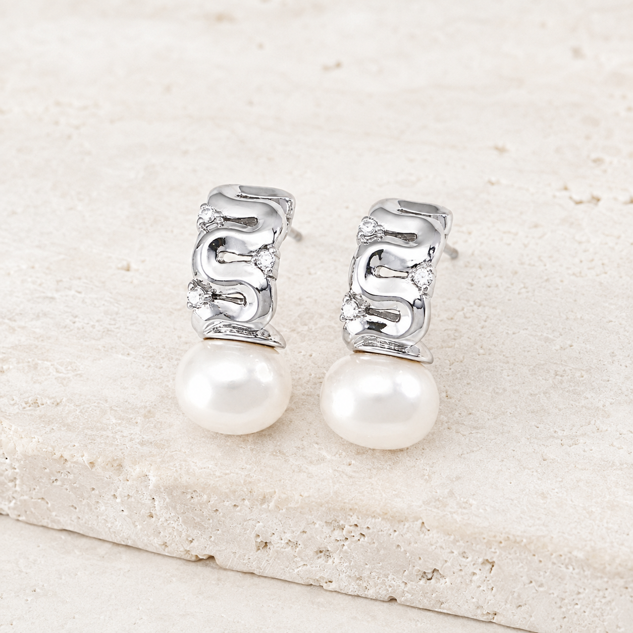 Silver pearl ribbon stud earrings with cubic zirconia on a stone display
