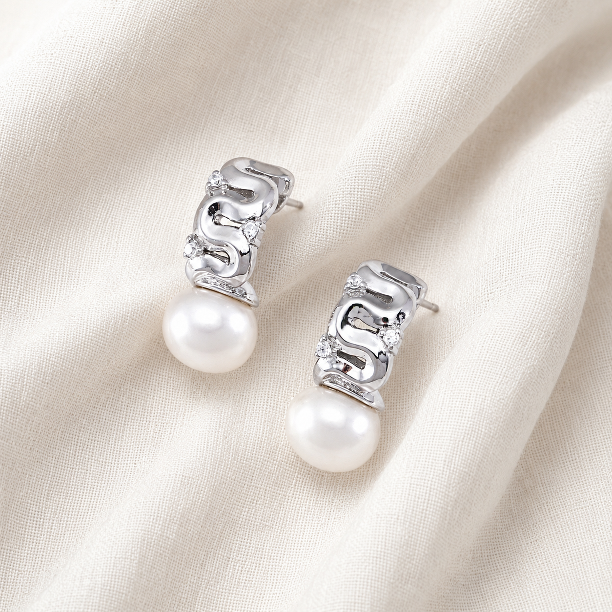 Pair of Silver pearl ribbon stud earrings with cubic zirconia on ivory fabric