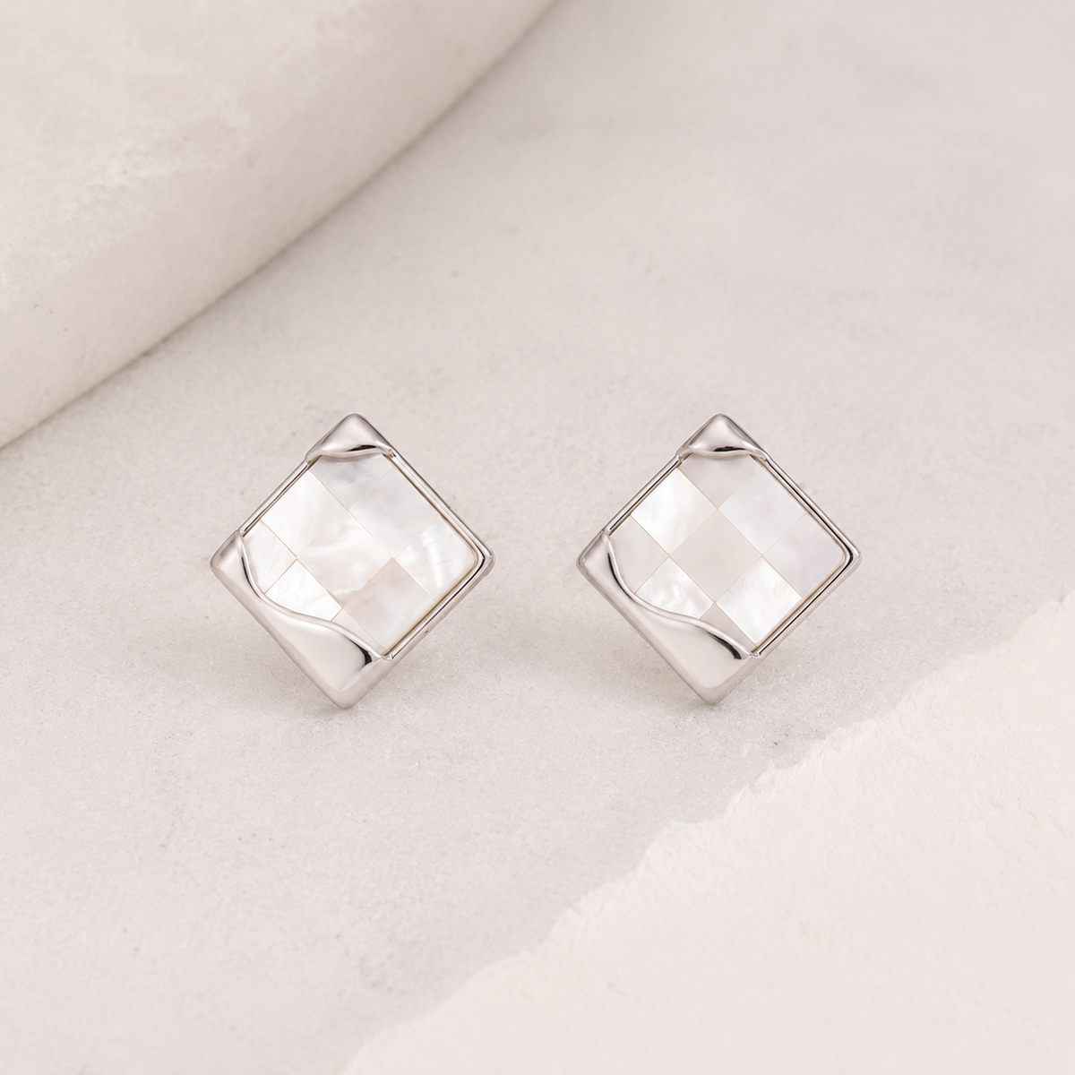 Silver shell mosaic stud earrings on an ivory surface