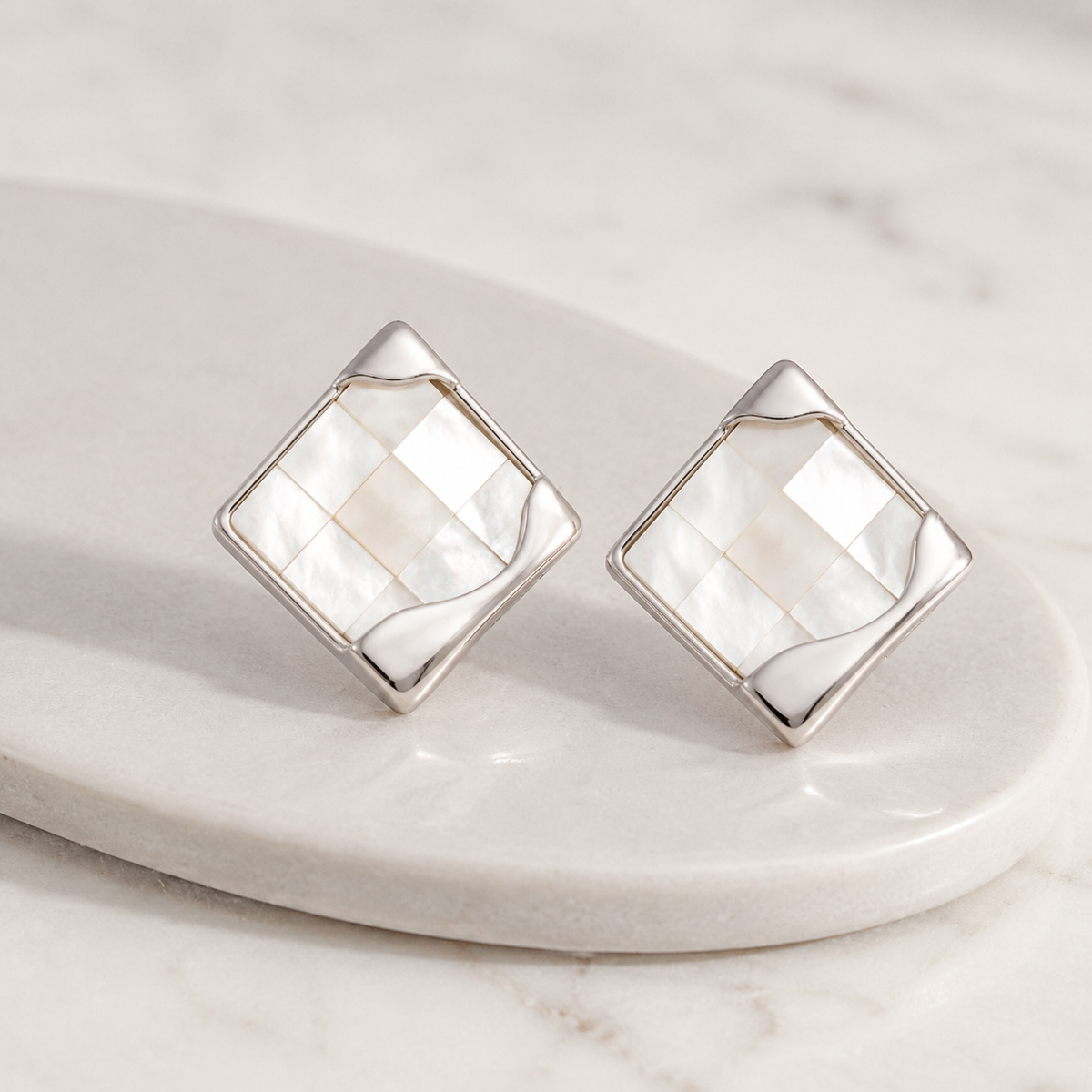 Silver shell mosaic stud earrings on a marble display