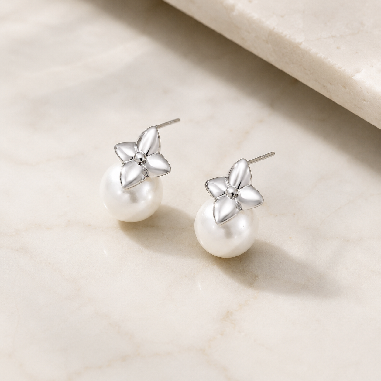 Silver four-leaf shell pearl stud earrings on an ivory display