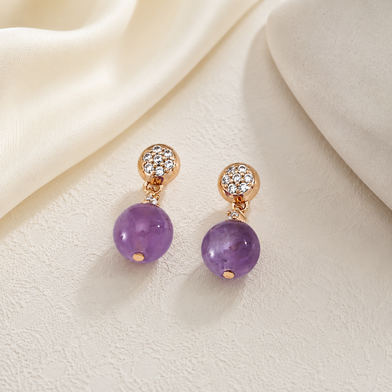 Pair of Amethyst Drop Earrings with cubic zirconia on an ivory textile display