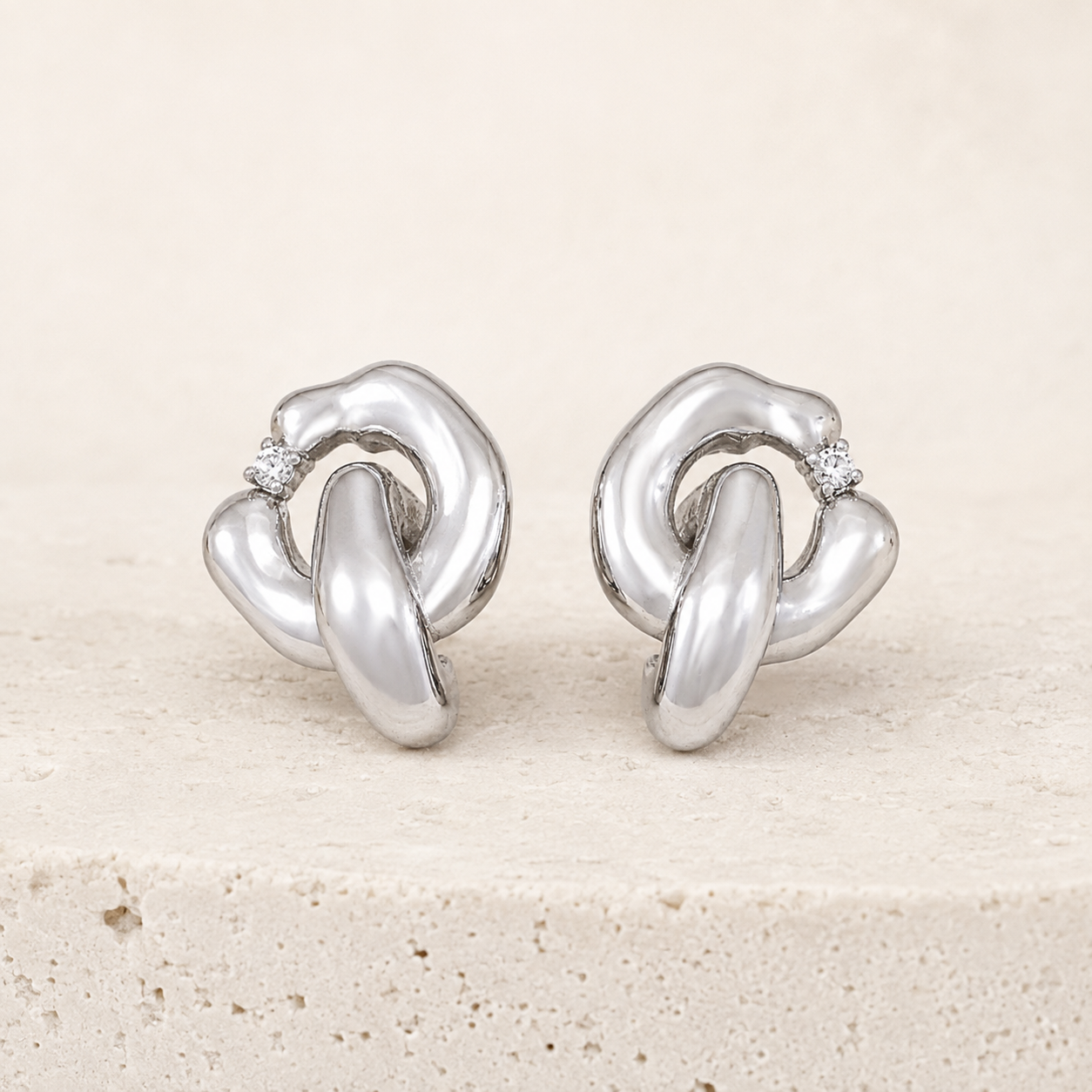 Pair of Silver Interlocking Zircon Earrings on a stone display