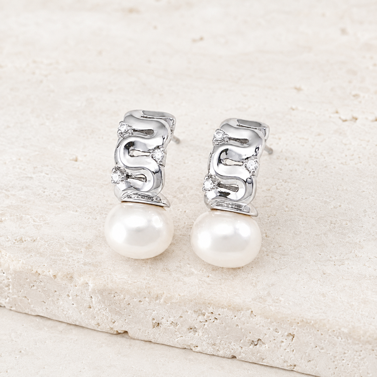 Silver pearl ribbon stud earrings with cubic zirconia on a stone display