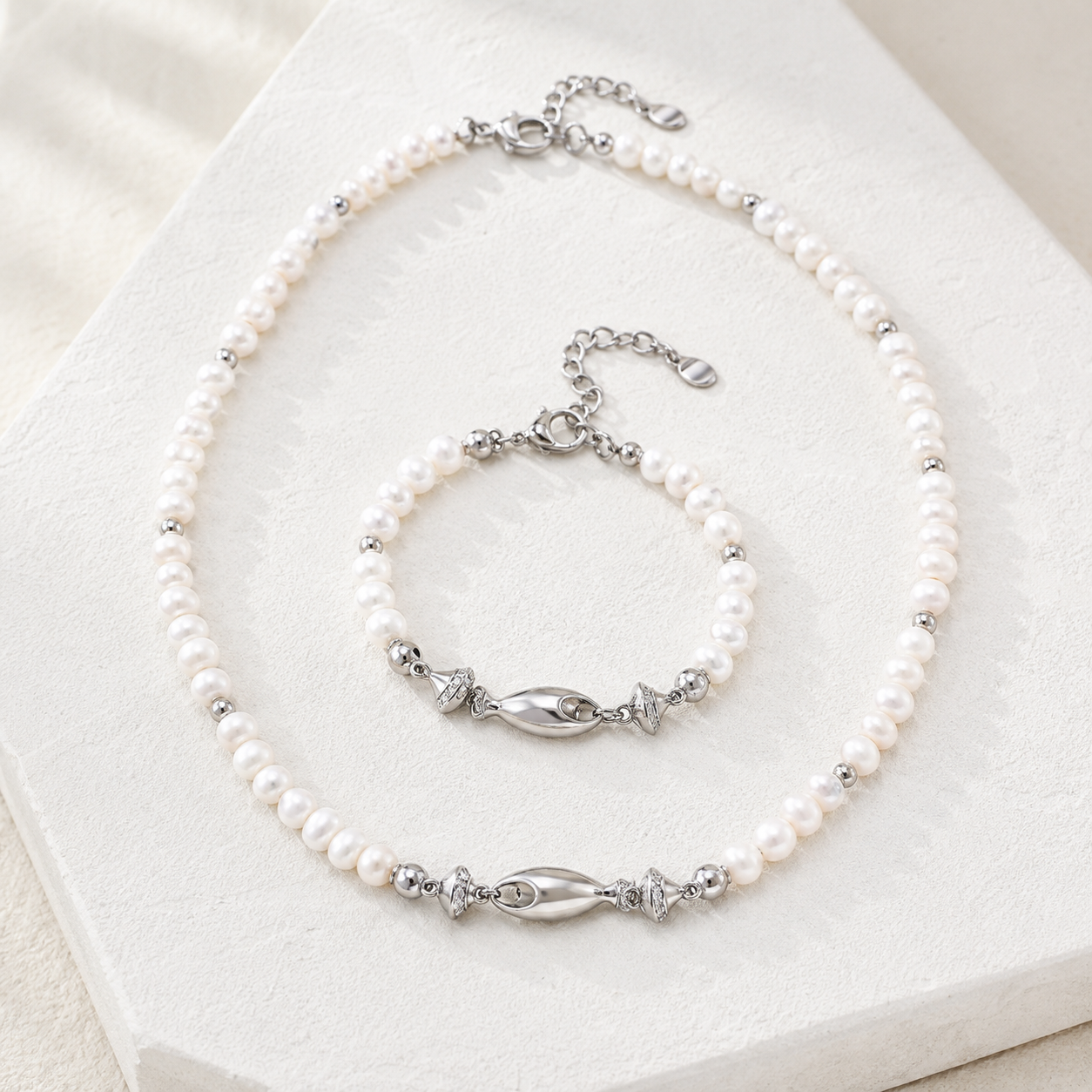 Silver natural pearl fish necklace and bracelet set on an ivory display