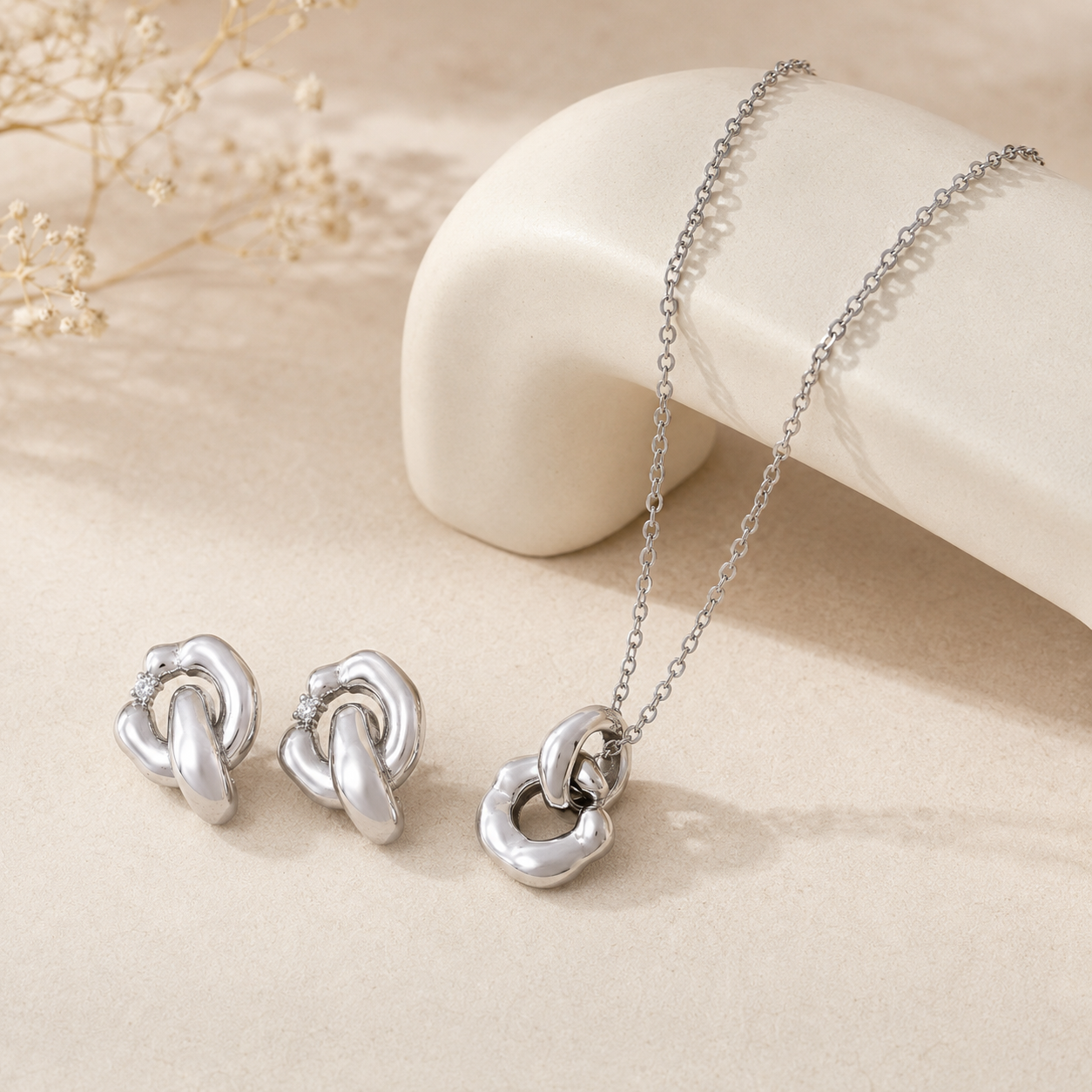 Silver Interlocking Jewelry Set with pendant necklace and cubic zirconia earrings on an ivory display