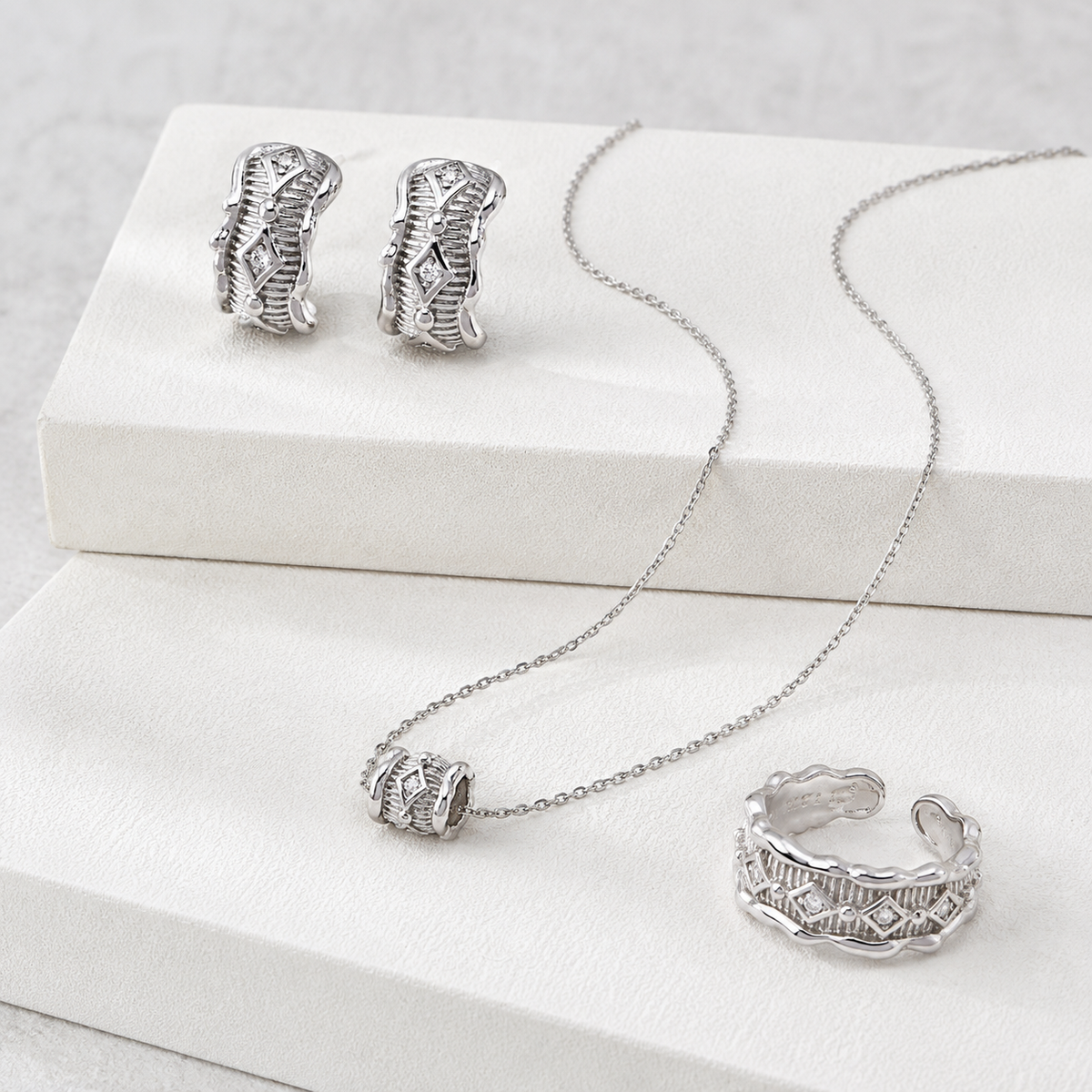 Silver zircon jewelry set with ring, pendant necklace, and stud earrings on white displays