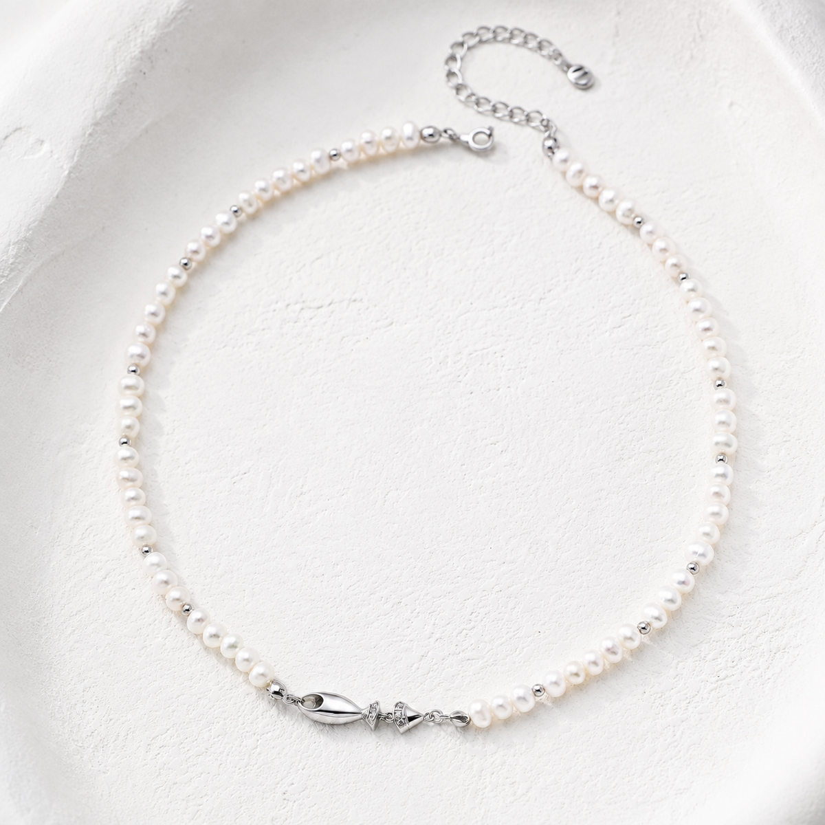 Silver natural pearl fish necklace on a white textured background