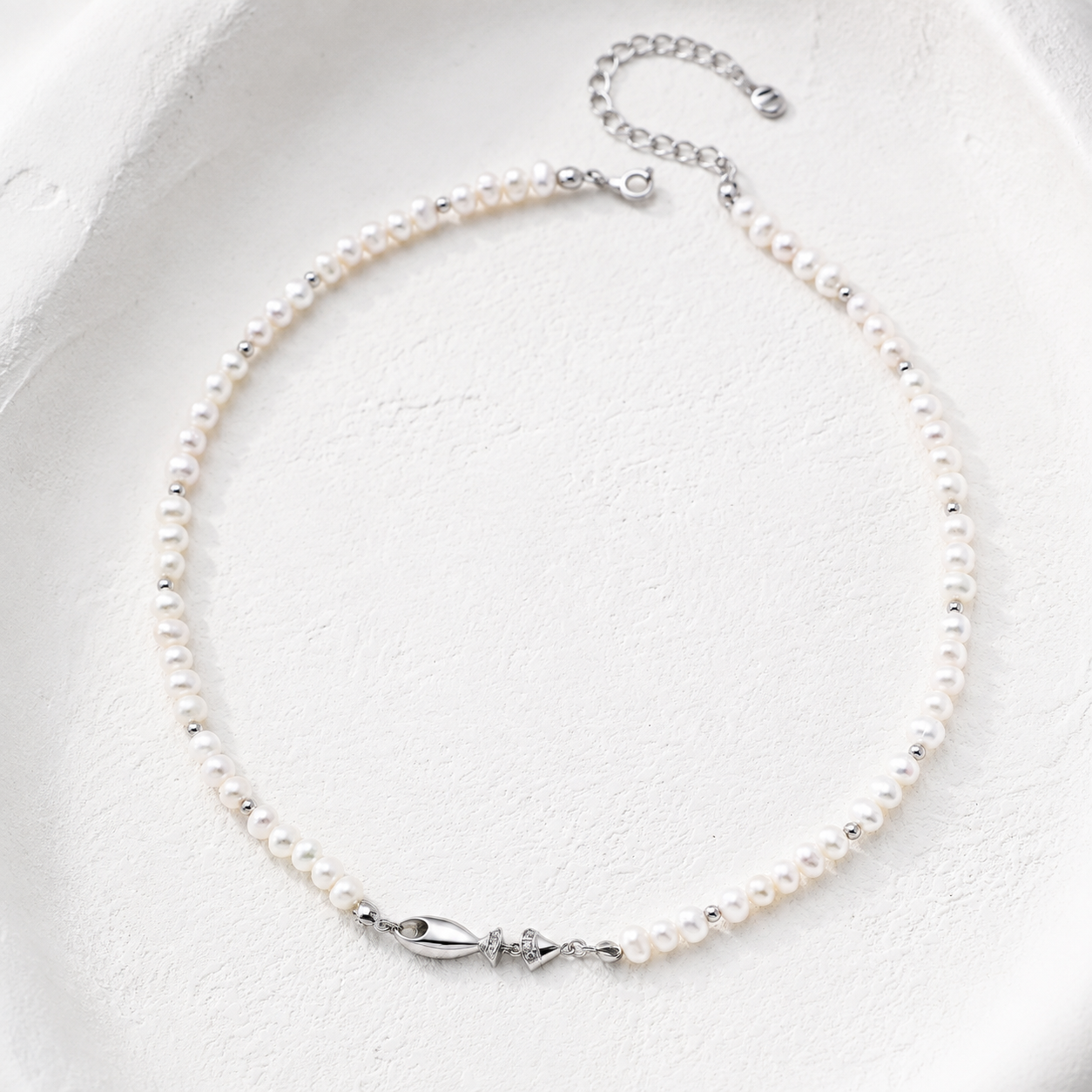 Silver natural pearl fish necklace on a white textured background