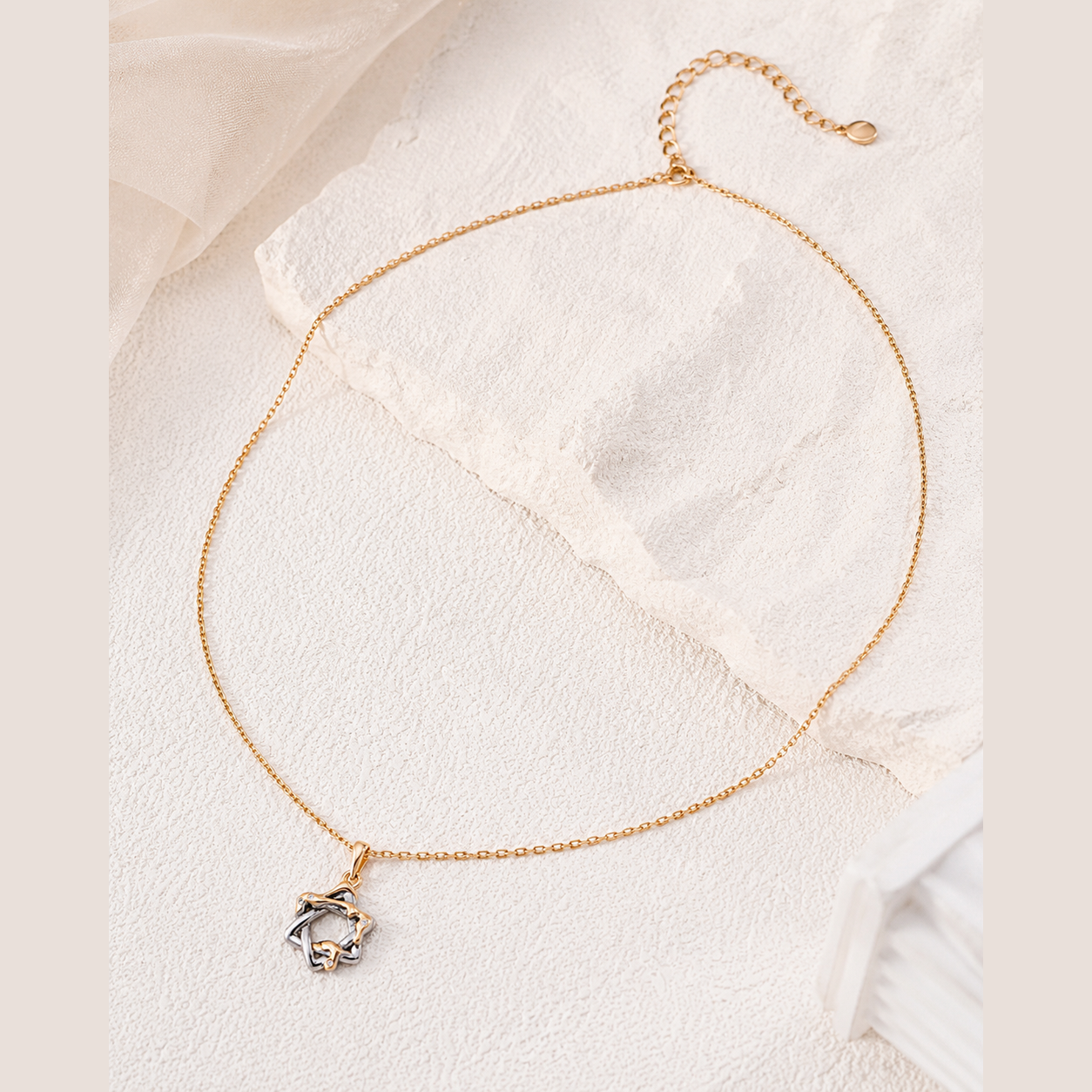 Interwoven Star Pendant Necklace in Vintage Gold laid on an ivory stone display